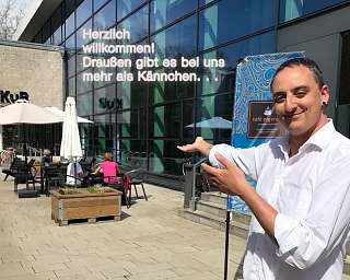 Ein Mann zeigt auf ein Willkommensschild vor einem Café.