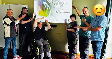 Sechs Personen zeigen auf eine Präsentation mit dem Titel Zertifikatslehrgang.